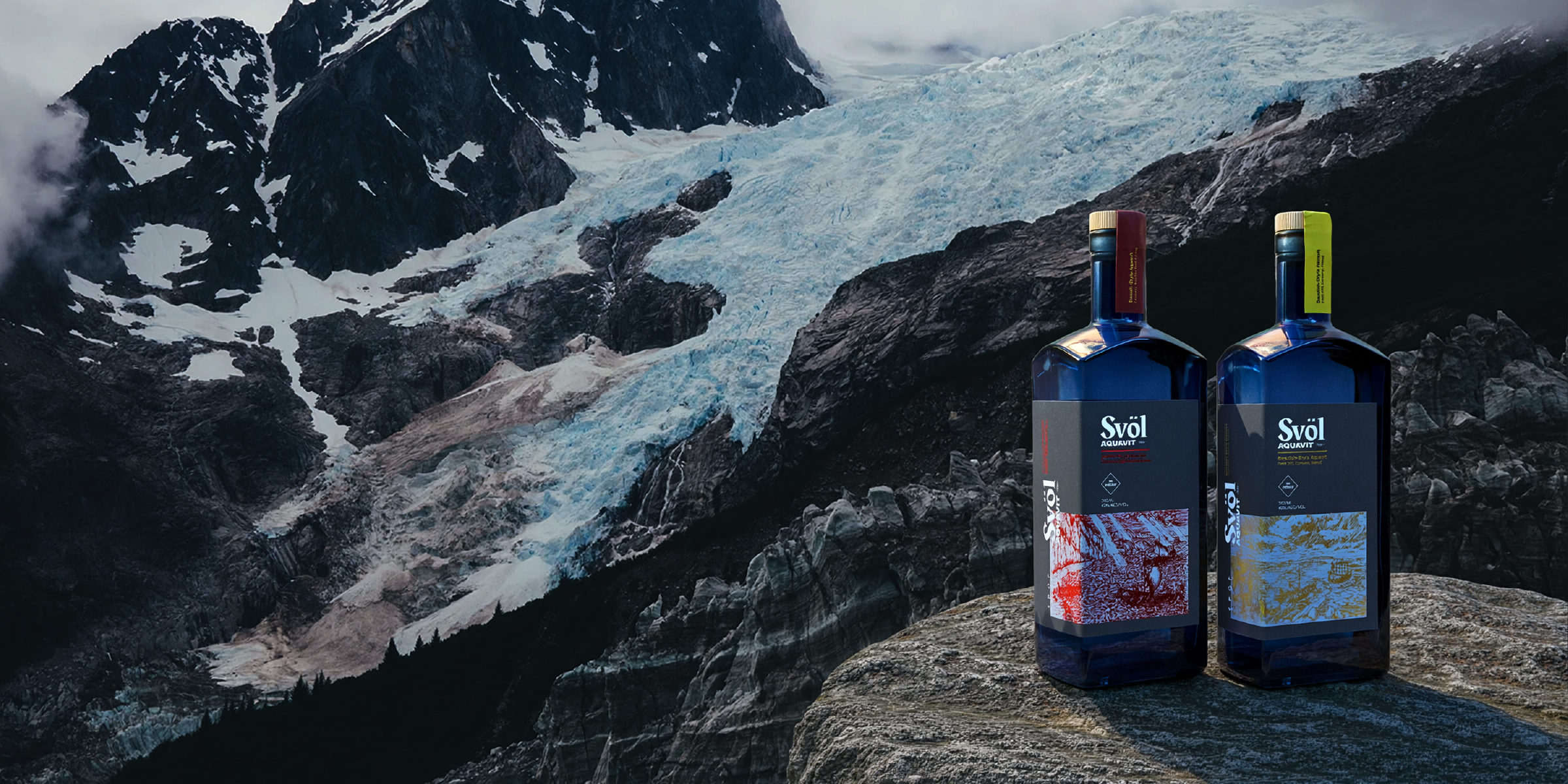 Svöl Danish-Style and Swedish-Style Aquavit bottles on a rock ledge in front of a glacier and dark mountains